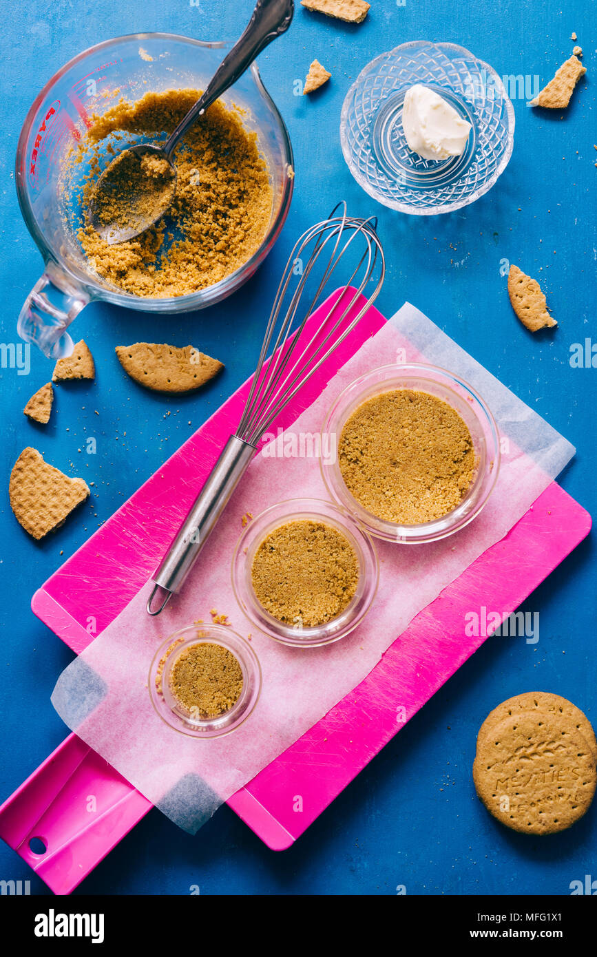 Plastic circular   cntainer are filled with granulated biscuits and butter then pressed to ccreate the base of chesecake dessert, cooking concept, ove Stock Photo