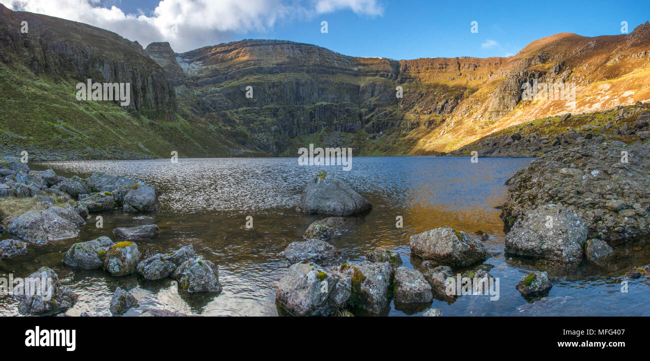 Amazing view from the valley bottom of Coumshingaun lake, boulders and rocks, and the steep cliffs, mountain walls. Irish landscapes, rugged terrain. Stock Photo