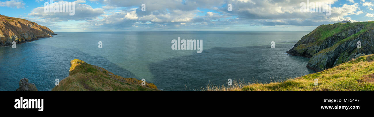 Panoramic view to the horizon of the open Irish sea, from Howth Head in Ireland. Lighthouse atop the cliff, cloudy sky and deep blue sea at sunset. Stock Photo