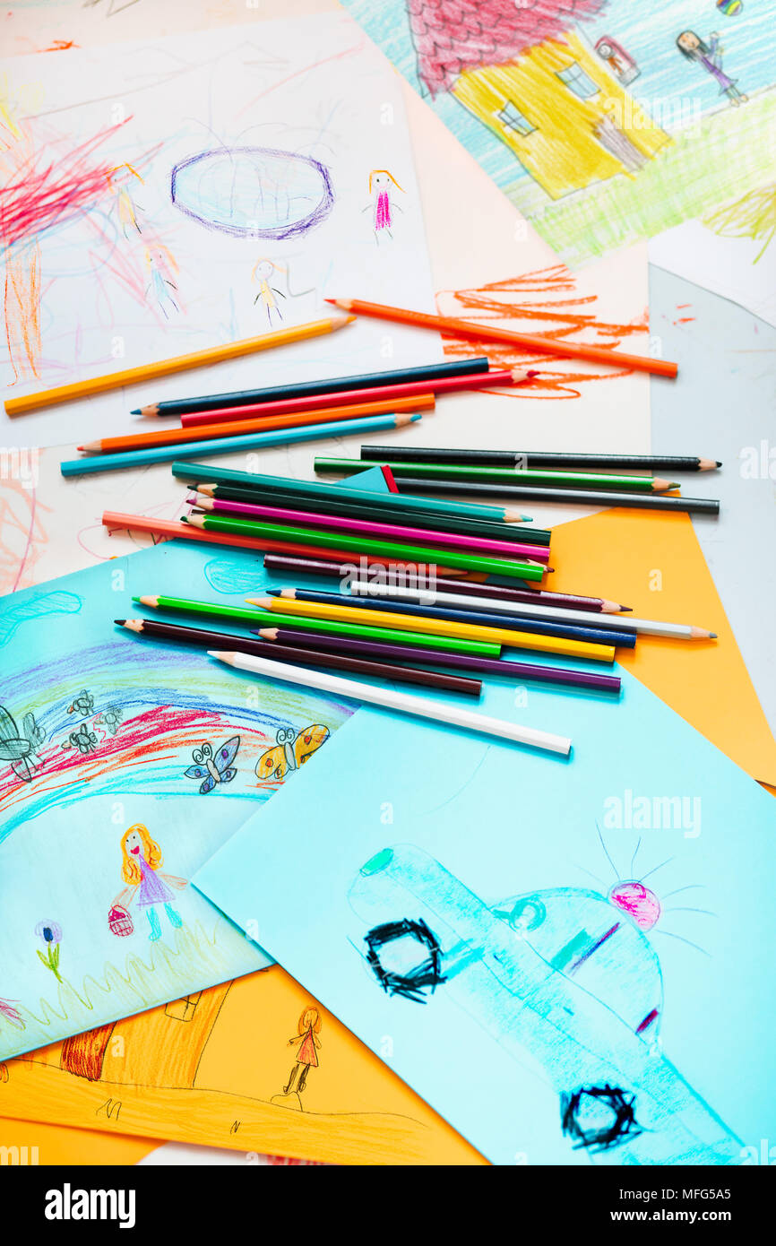 Pencil crayons scattered on desktop filled with colorful childlike drawings of playing children, house, car. Photo from above Stock Photo
