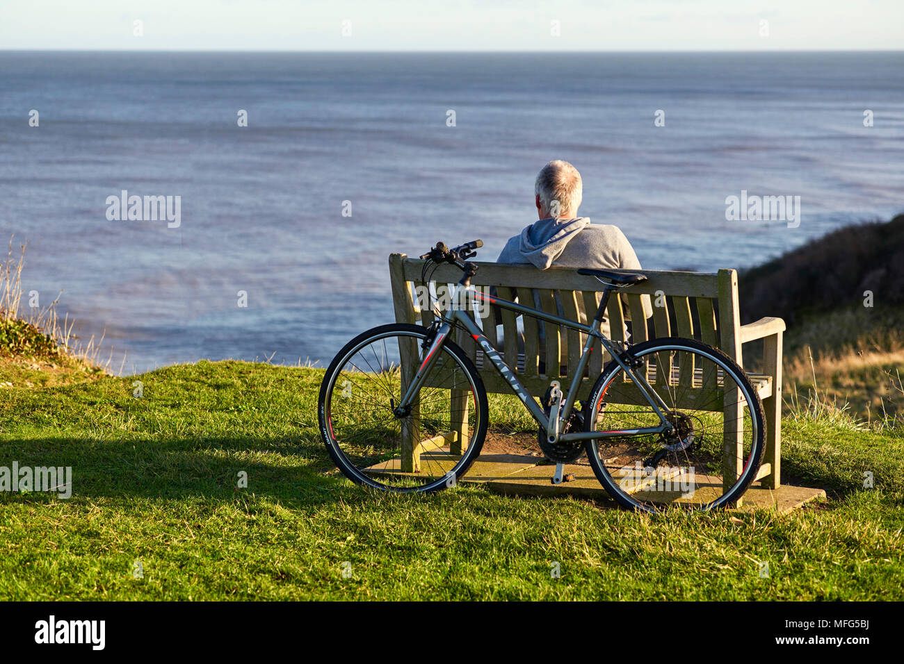 Older male cyclist having a rest on a bench overlooking the sea at Overstrand, Norfolk Stock Photo