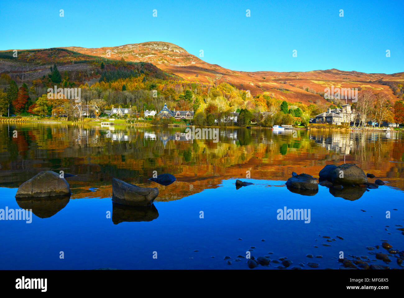 Looking across Loch Earn to St Fillans village, Scotland UK  Autumn colours and reflections clear blue sky sunny day October 2017 Stock Photo