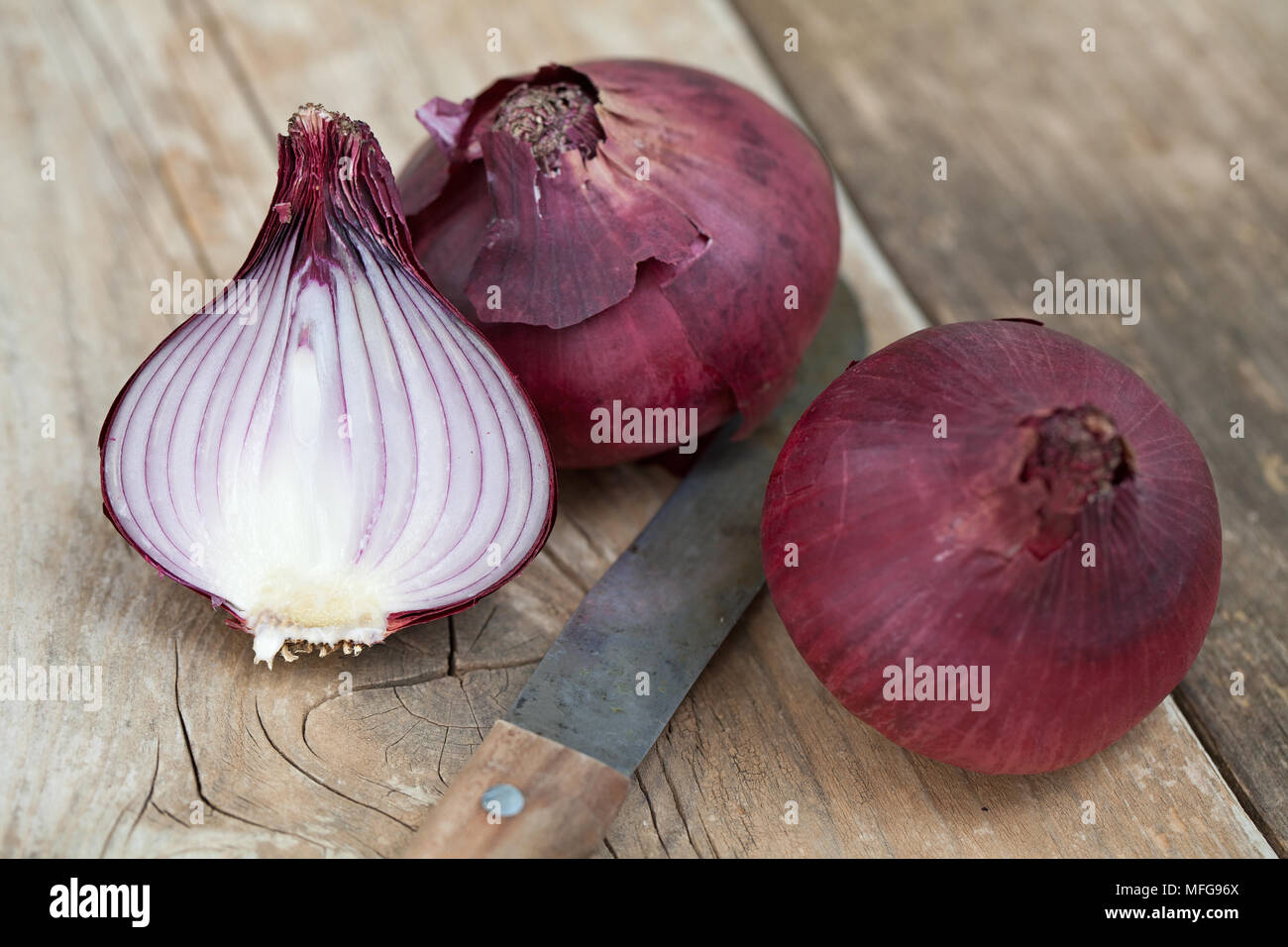 Two whole and a half red onions on a cutting board with a kitchen knife ...