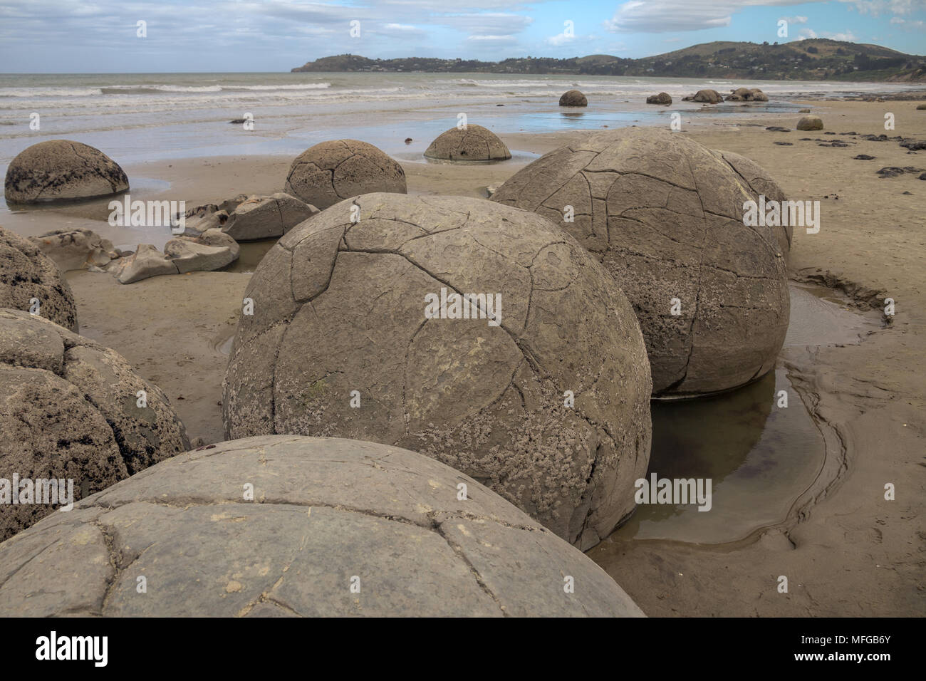 A giant ball shaped boulder almost covered in sand on the beach at Moeraki  South Island New Zealand Stock Photo - Alamy