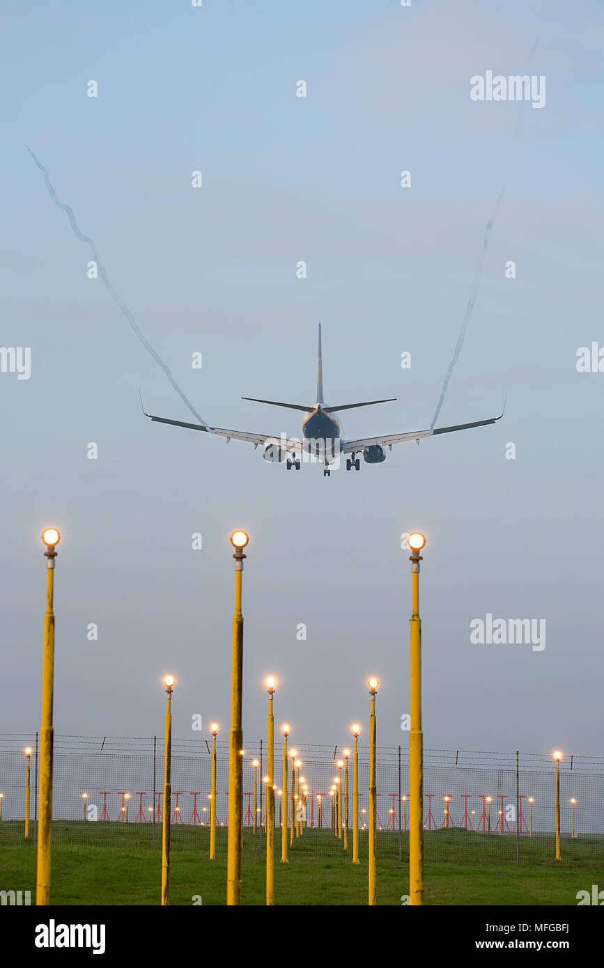 The rear of a landing commercial airplane with landing gear down viewed through rows of runway landing lights. Stansted International Airport, England Stock Photo