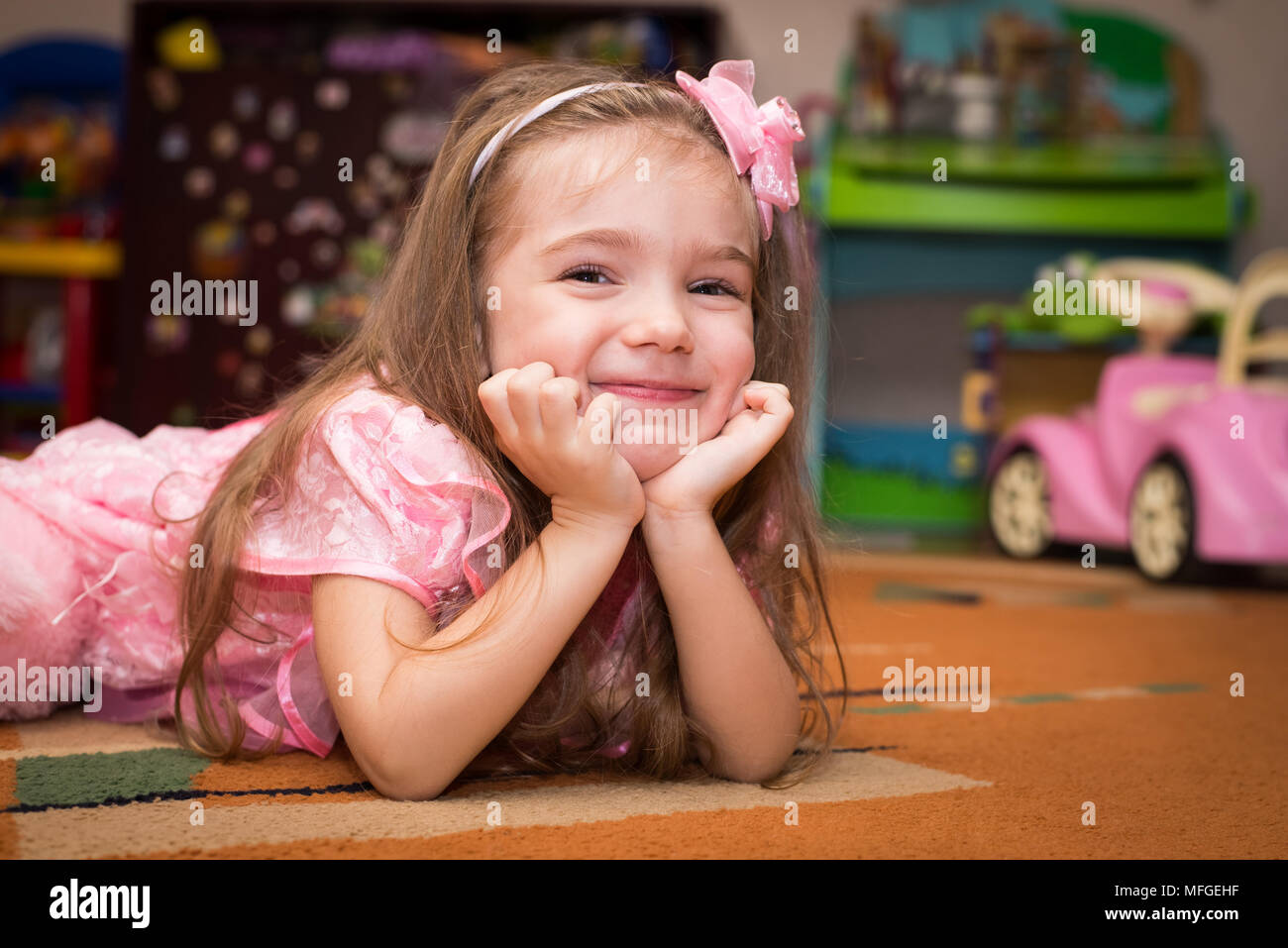 Little girl in a pink dress lies on the floor with a toy Stock Photo ...
