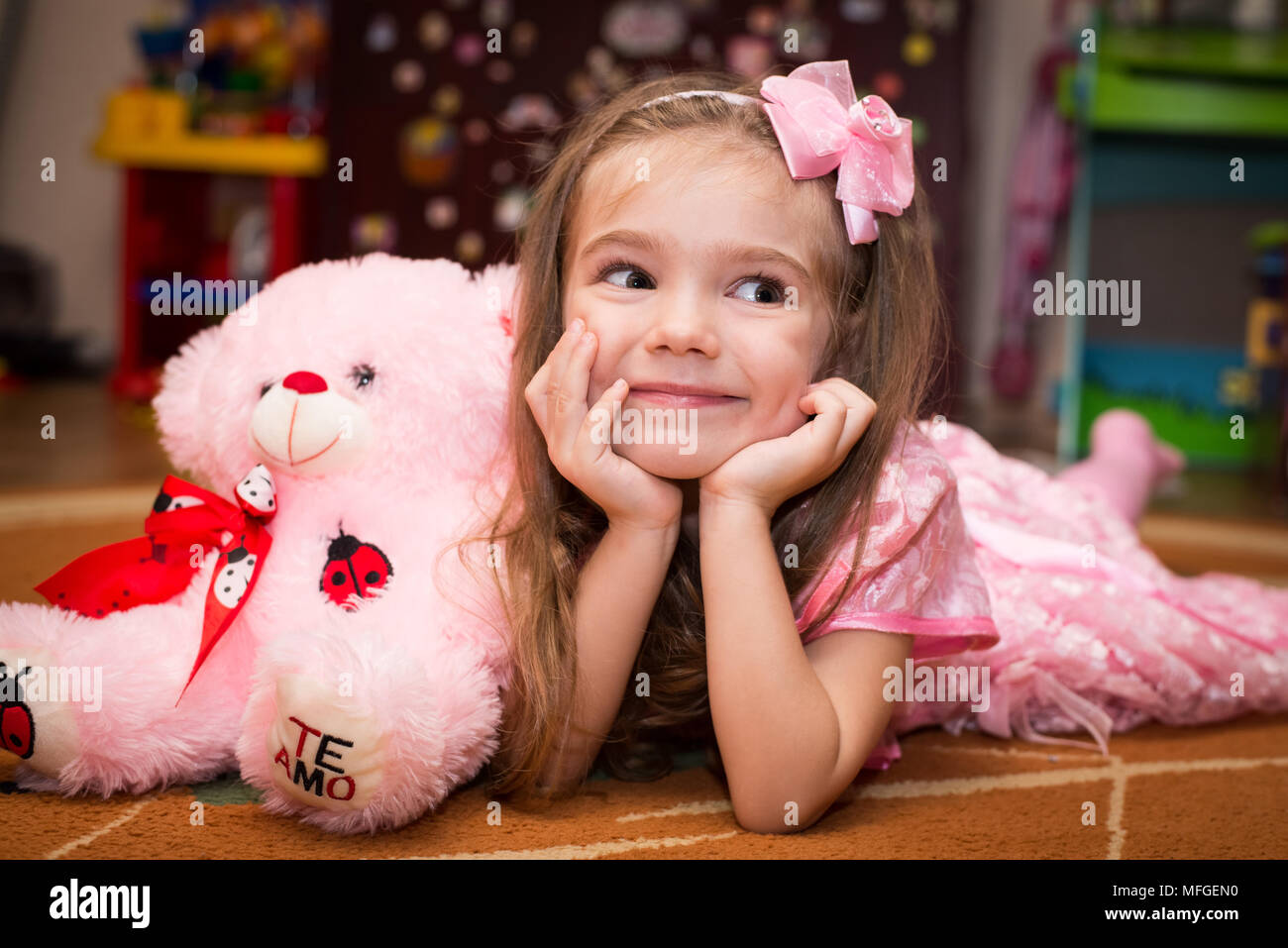 Little girl in a pink dress lies on the floor with a toy Stock Photo ...