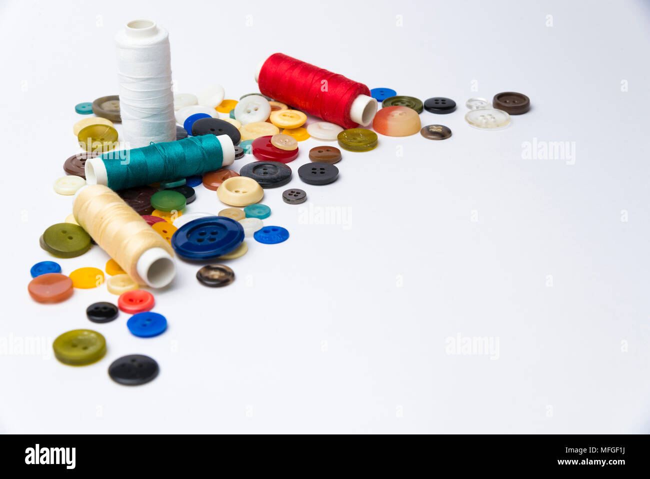 multi-colored buttons and coils with threads lie on a white surface Stock Photo