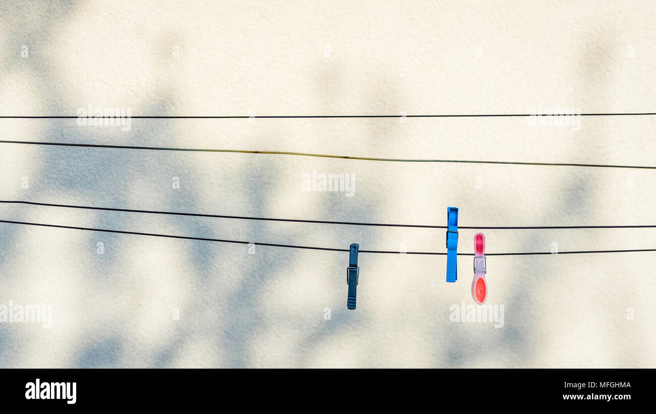 Clothing pins hanging on washing lines with a clear wall as background, with copy space. Stock Photo