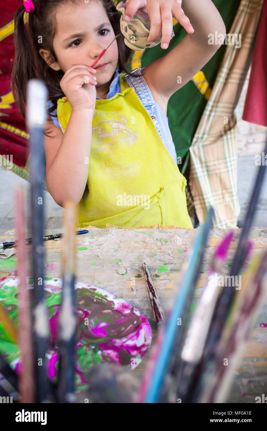 Child girl painting little clay piece. Ceramic workshop for children concept Stock Photo