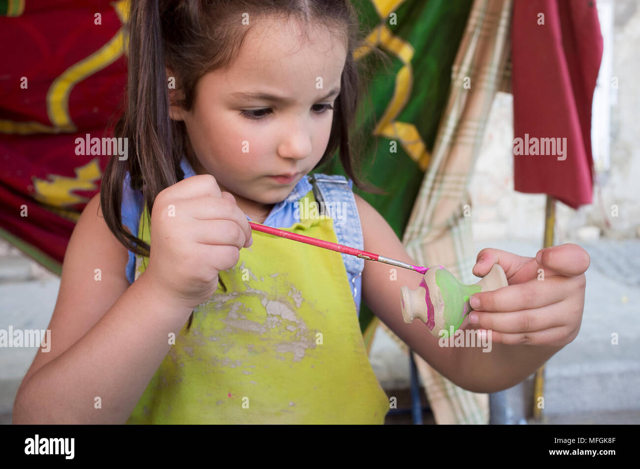 Child girl painting little clay piece with purple. Ceramic workshop for children concept Stock Photo