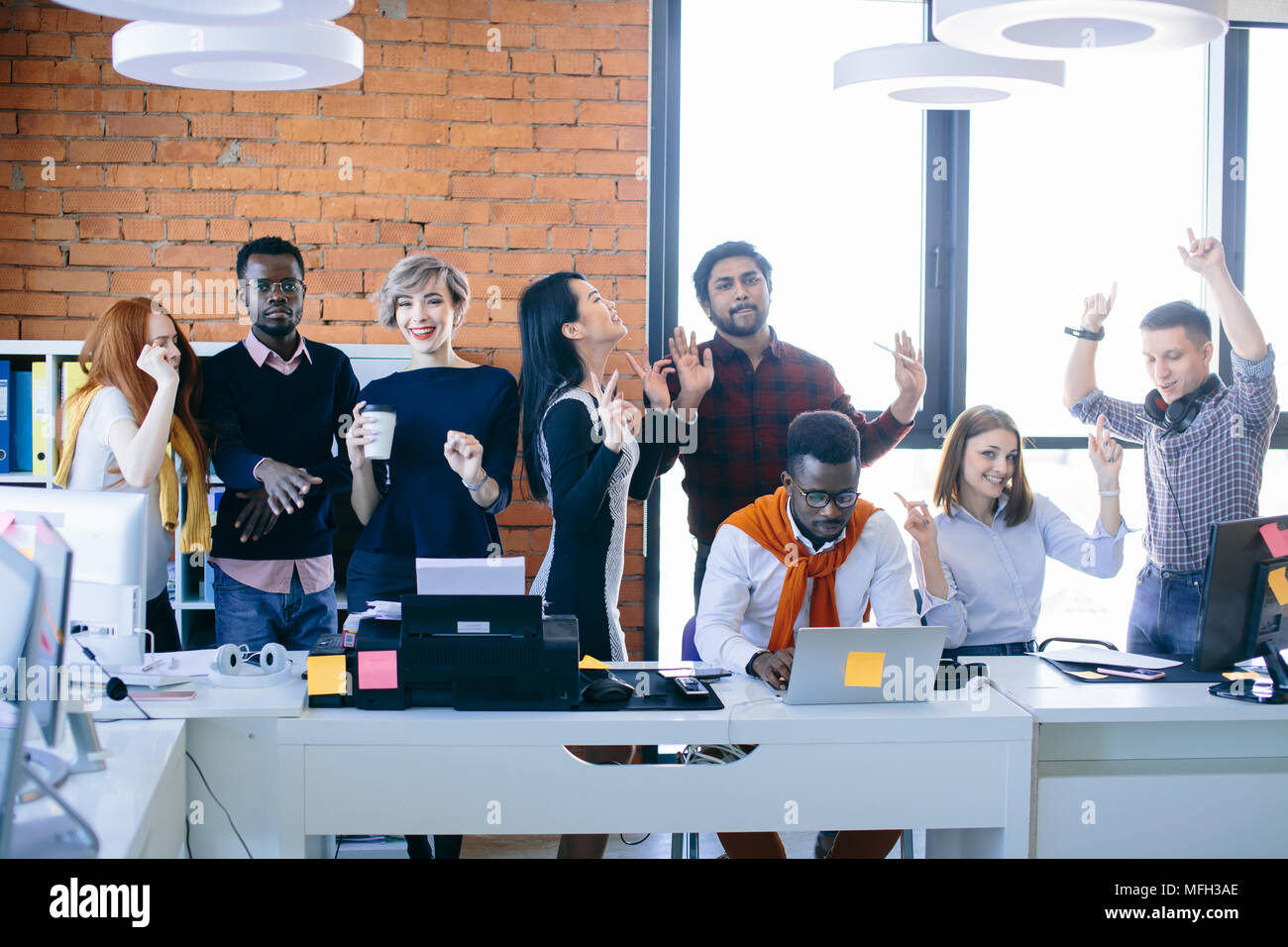 African student is trying to concentrate on his work with laptop while his friends are dancing and having fun. divert attention Stock Photo