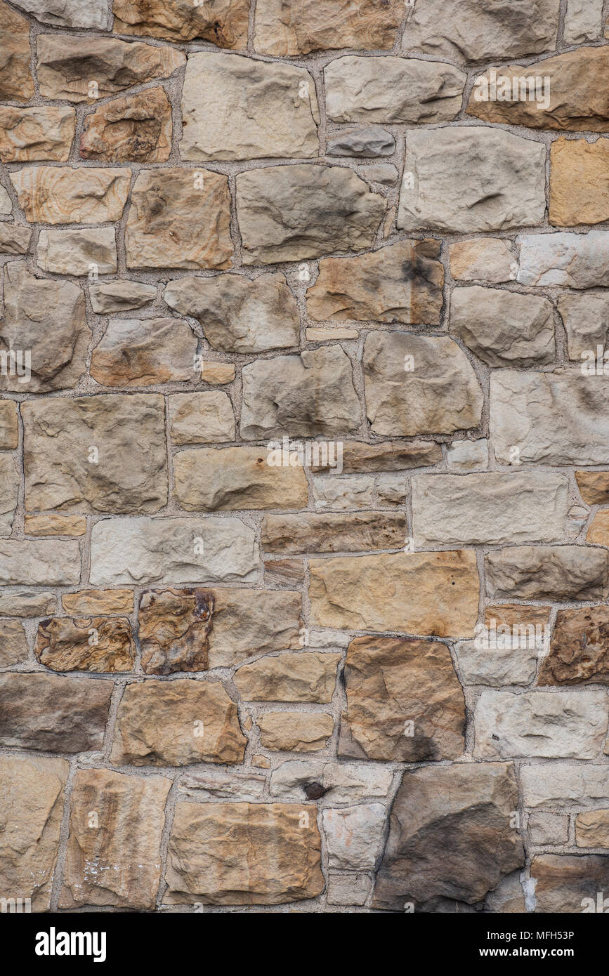 Building wall unevenly composed of earth-toned medium-size non-uniform rough-hewn stones of different shapes and sizes Stock Photo