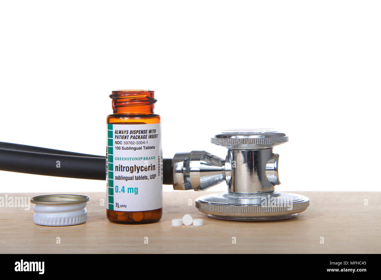 Alameda, CA - April 18, 2018: Bottle of Nitroglycerin tabs on wood table with 3 pills next to bottle and stethoscope. Nitro is used to treat episodes  Stock Photo
