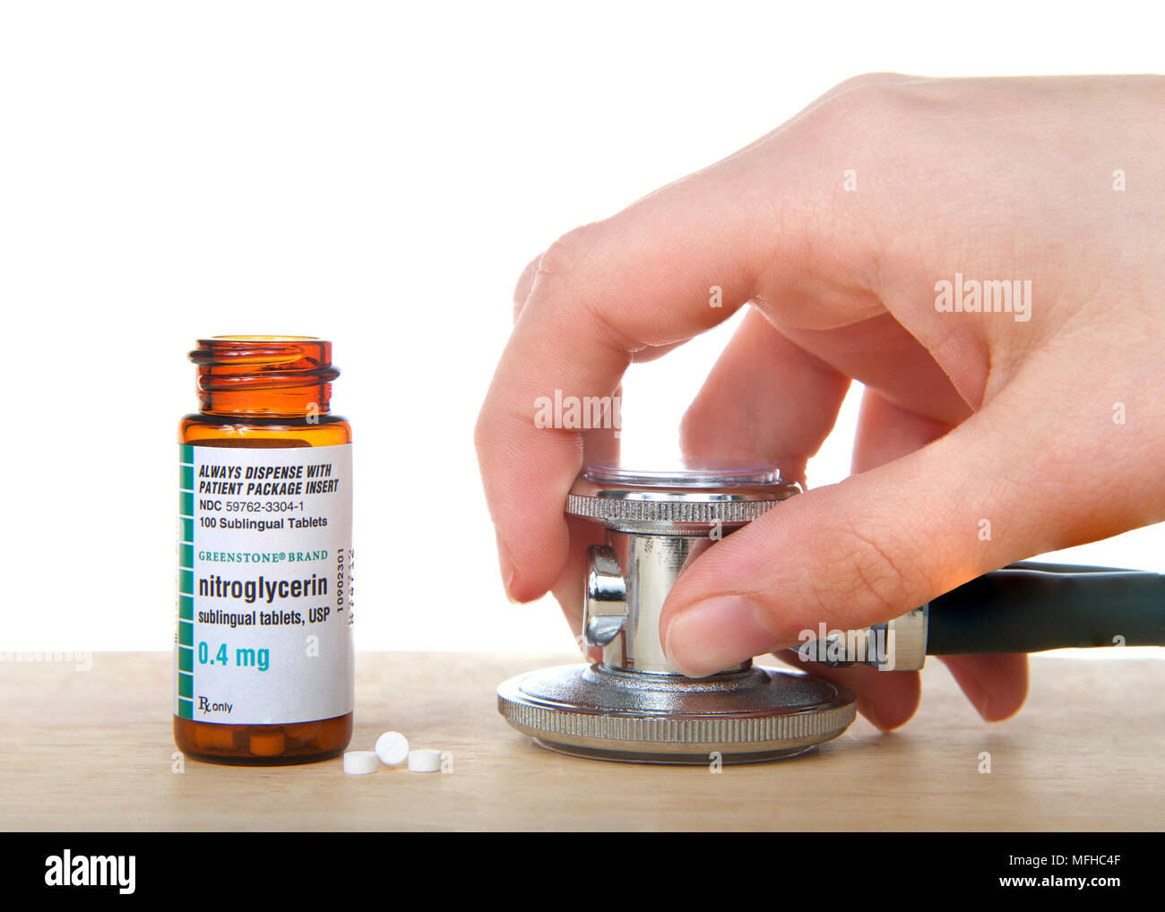 Alameda, CA - April 18, 2018: Bottle of Nitroglycerin tabs on wood table with 3 pills next to bottle and hand holding stethoscope. Nitro is used to tr Stock Photo