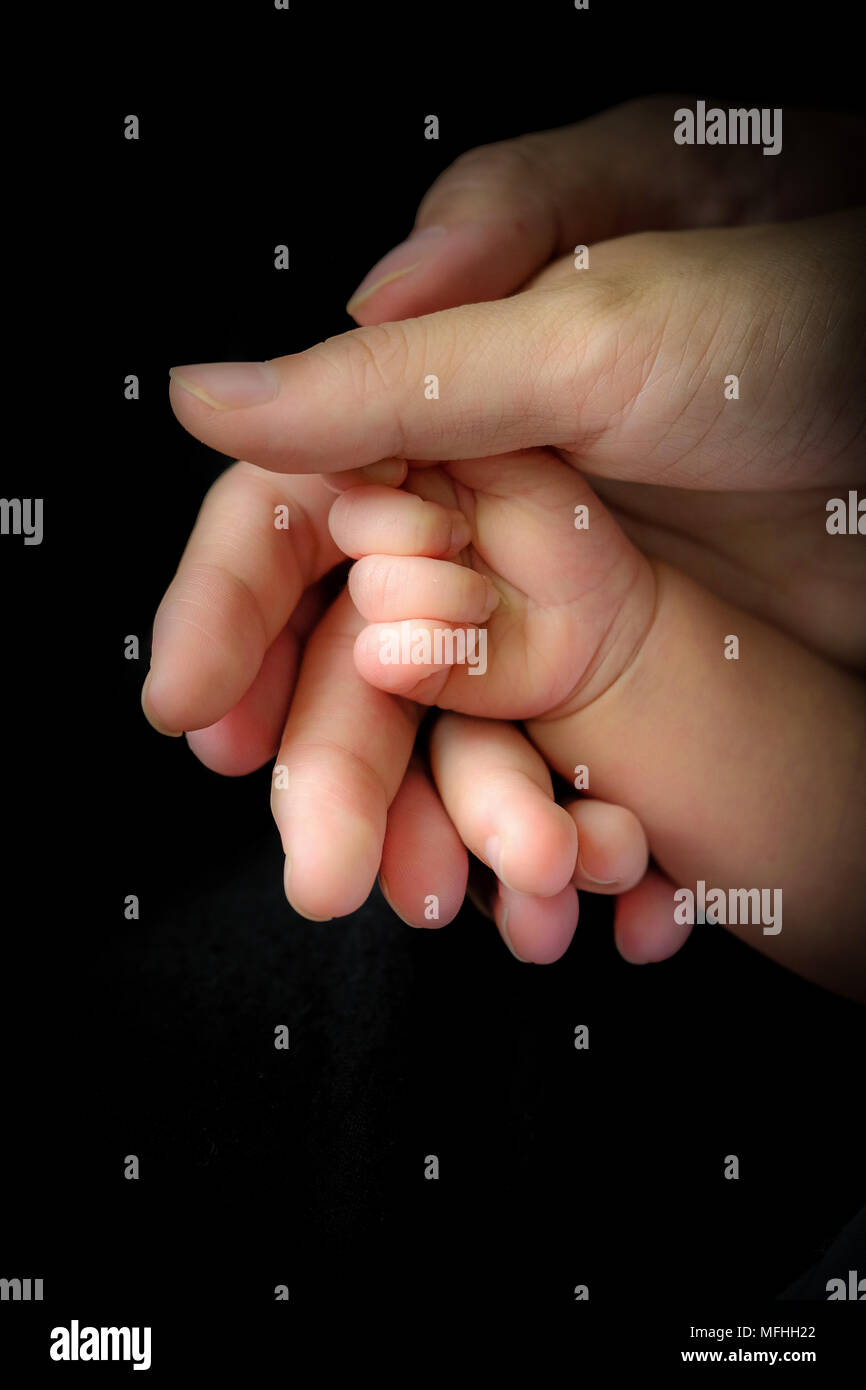 Hopeful feeling close-up of mother's and father's hands holding newborn baby. Stock Photo