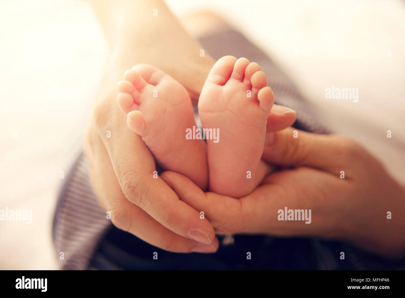 Newborn Baby Feet in mother hands with soft sunlight. conceptual image of maternity Stock Photo