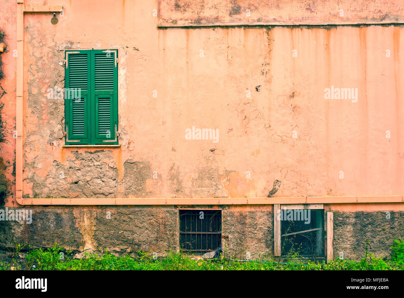 Small window with closed green shutters on an old and weathered empty pastel pink wall Stock Photo