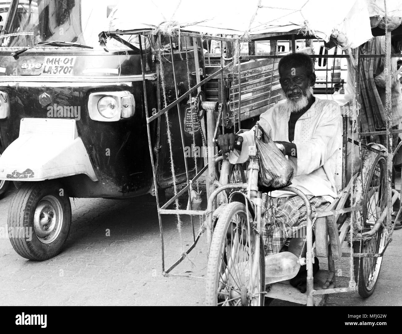 Old man amputee competing with the traffic on a hand powered rickshaw on a Mumbai street, India Stock Photo