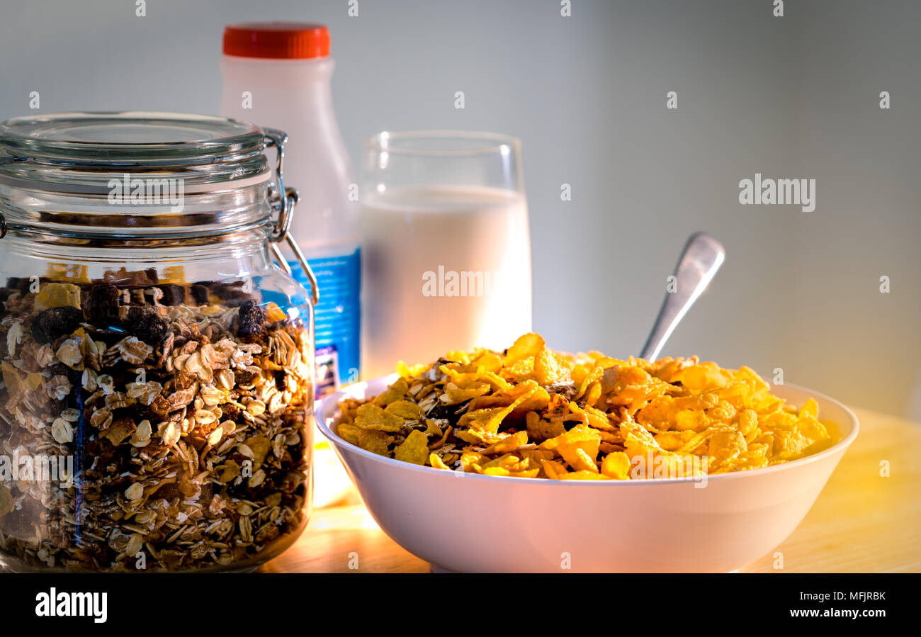 Bowl of cereal with spoon put on wood table near granola in glass