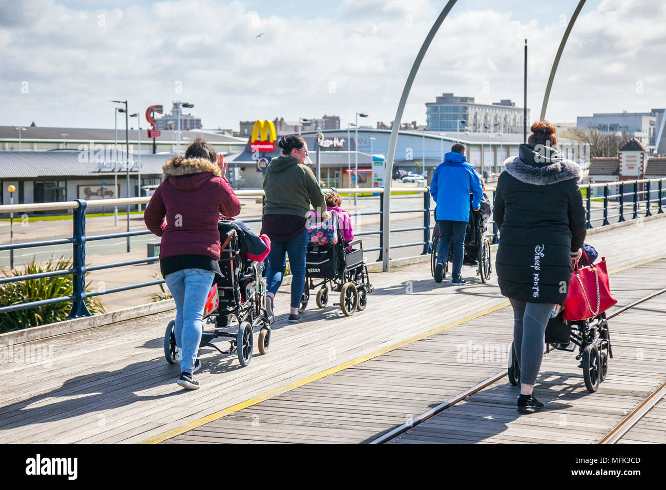 Wheelchair user at Southport, Merseyside. UK Weather. 26/04/2018.  Sunny, blustery day on the north-west coast as disabled people in wheelchairs are taken on a taken for a walk on the resorts Victorian Pier which is undergoing a refit. Workmen are engaged on a 2.9 million repair and enhancement of the iron structure, which is the 2nd longest pier remaining in England.  Credit: MedaiWorldImages/AlamyLiveNews. Stock Photo
