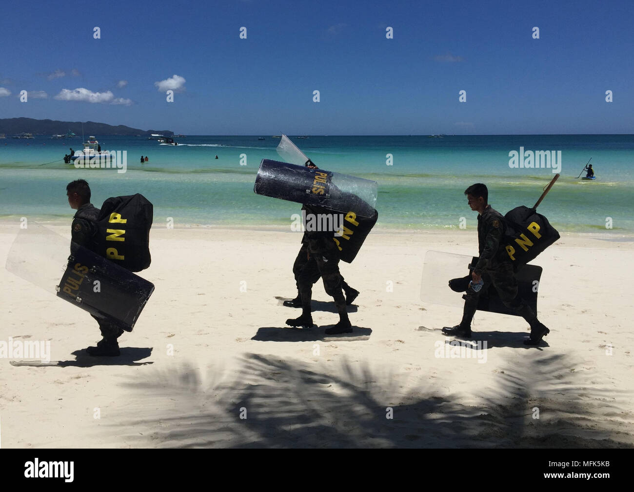 24 April 2018, Philippines, Boracay Island: A police officer walking behing tourists at white beach. A few weeks ago the island was still a dream goal. For some, the island was the most beautiful in the world. That is until the president of the Philippines called it a cesspit. At least the island is fully booked for the next six months. Photo: Girlie Linao/dpa Stock Photo