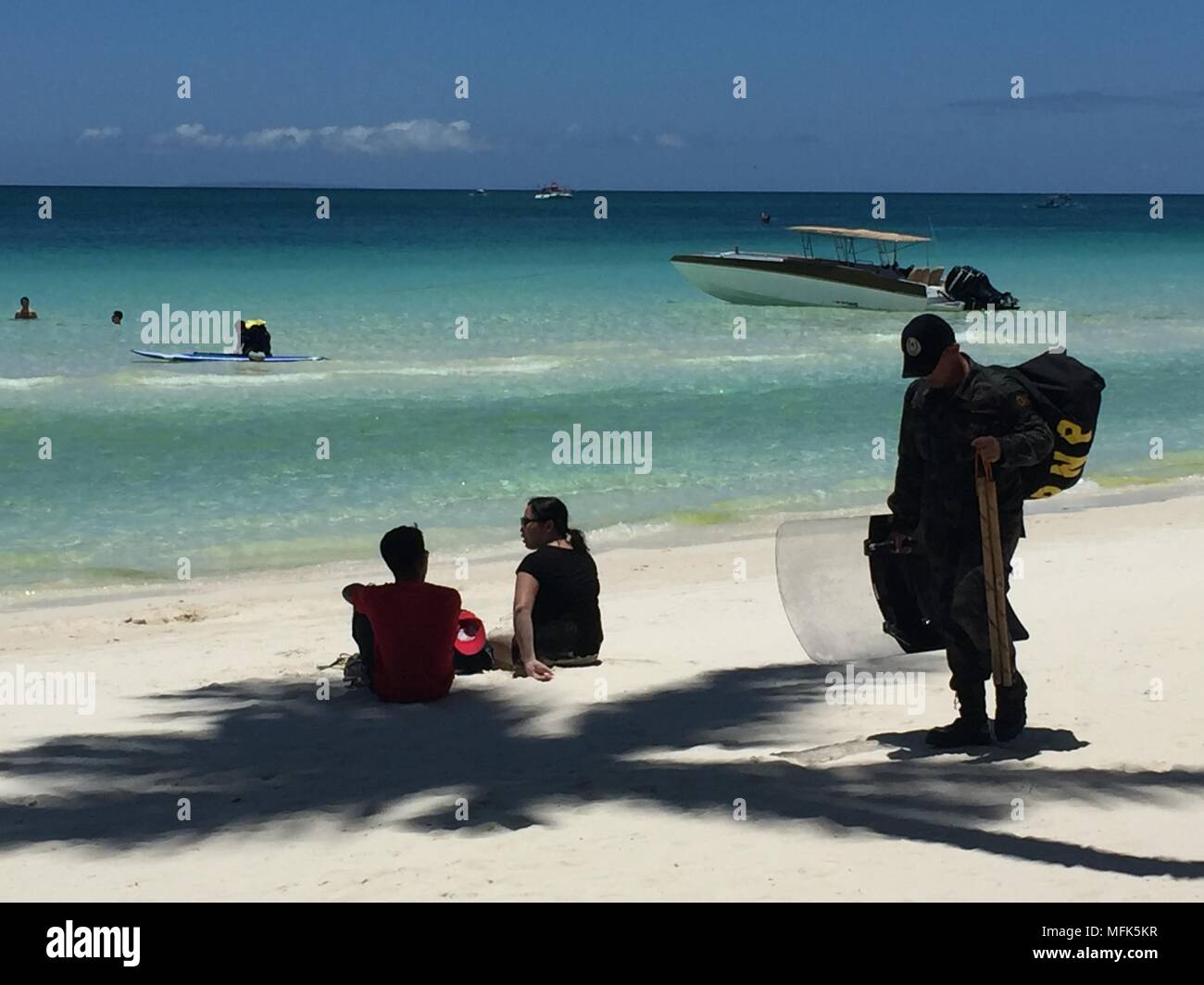 24 April 2018, Philippines, Boracay Island: A police officer walking behing tourists at white beach. A few weeks ago the island was still a dream goal. For some, the island was the most beautiful in the world. That is until the president of the Philippines called it a cesspit. At least the island is fully booked for the next six months. Photo: Girlie Linao/dpa Stock Photo