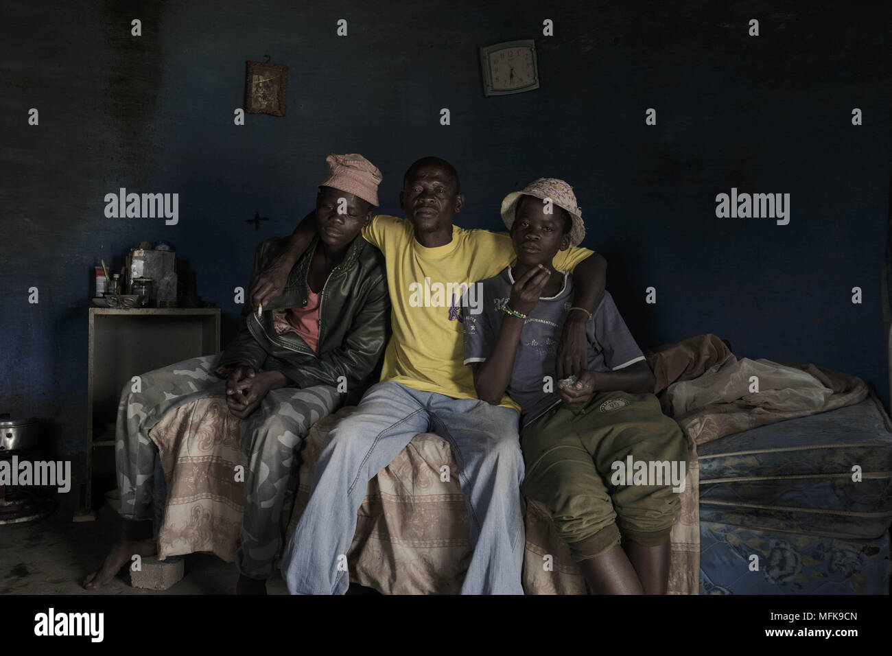 January 12, 2018 - Matatiele, Eastern Cape, South Africa - A father and heavy drinker, sits with his two suns Luis (14) and  Malike (18) on the bed in their mud house. The blue round shaped house serves as a sleeping room, community area and as a kitchen. (Credit Image: © Stefan Kleinowitz via ZUMA Wire) Stock Photo