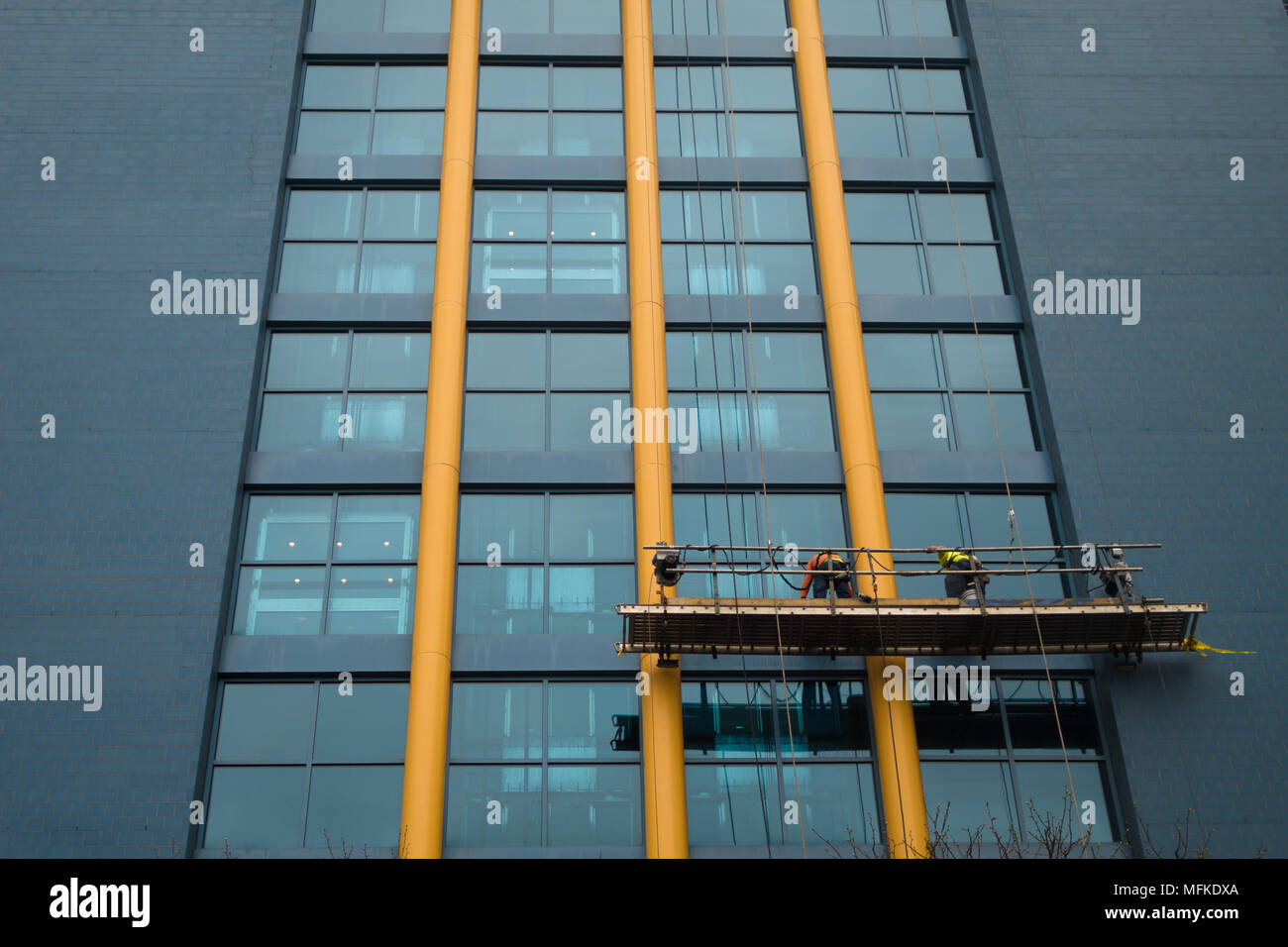 Two men work on an elevated platform cleaning windows on a blue building Stock Photo