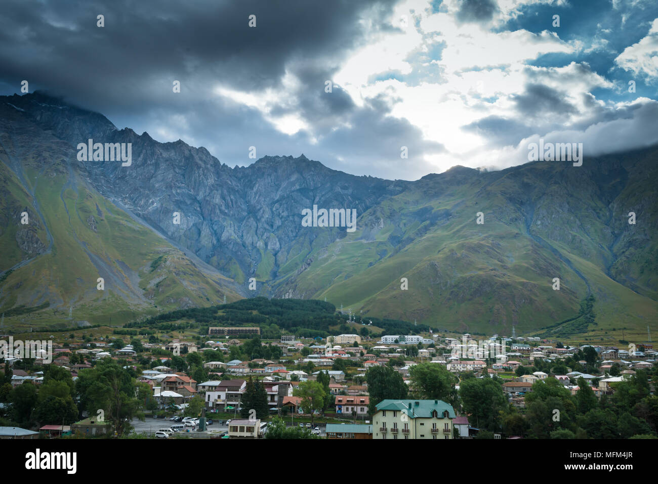 Beautiful landscape of majestic mountains, dramatic clouds and sky. View from the hill on village in the green valley Stock Photo