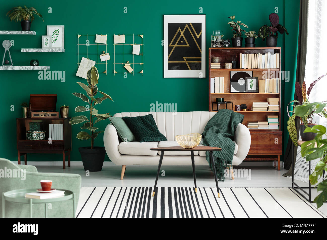 Modern design, botanic living room interior with cozy, beige sofa, antique furniture, home library, and teal green wall Stock Photo