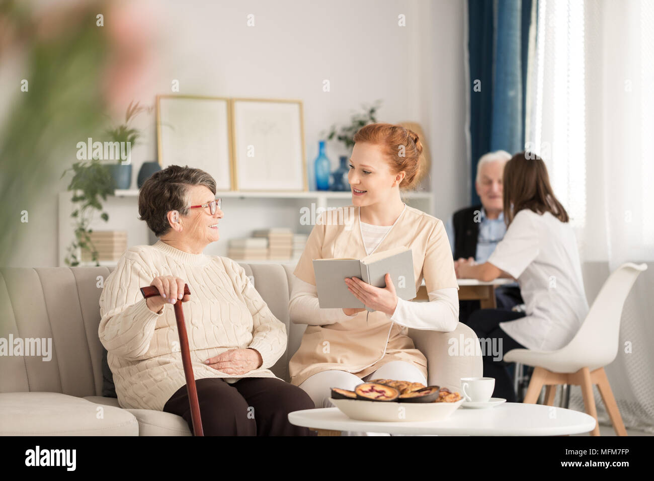 Professional caretaker in uniform reading a book to a happy senior