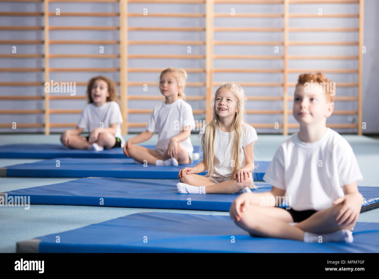 Focused pupils sitting cross-legged on blue mats during gymnastics class Stock Photo