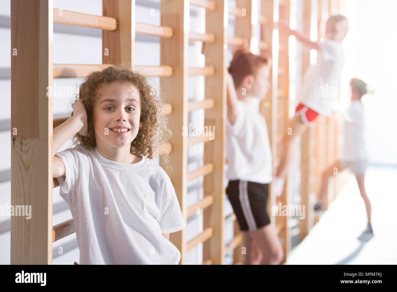 Smiling kid standing next to wall bars at sports hall during training Stock Photo