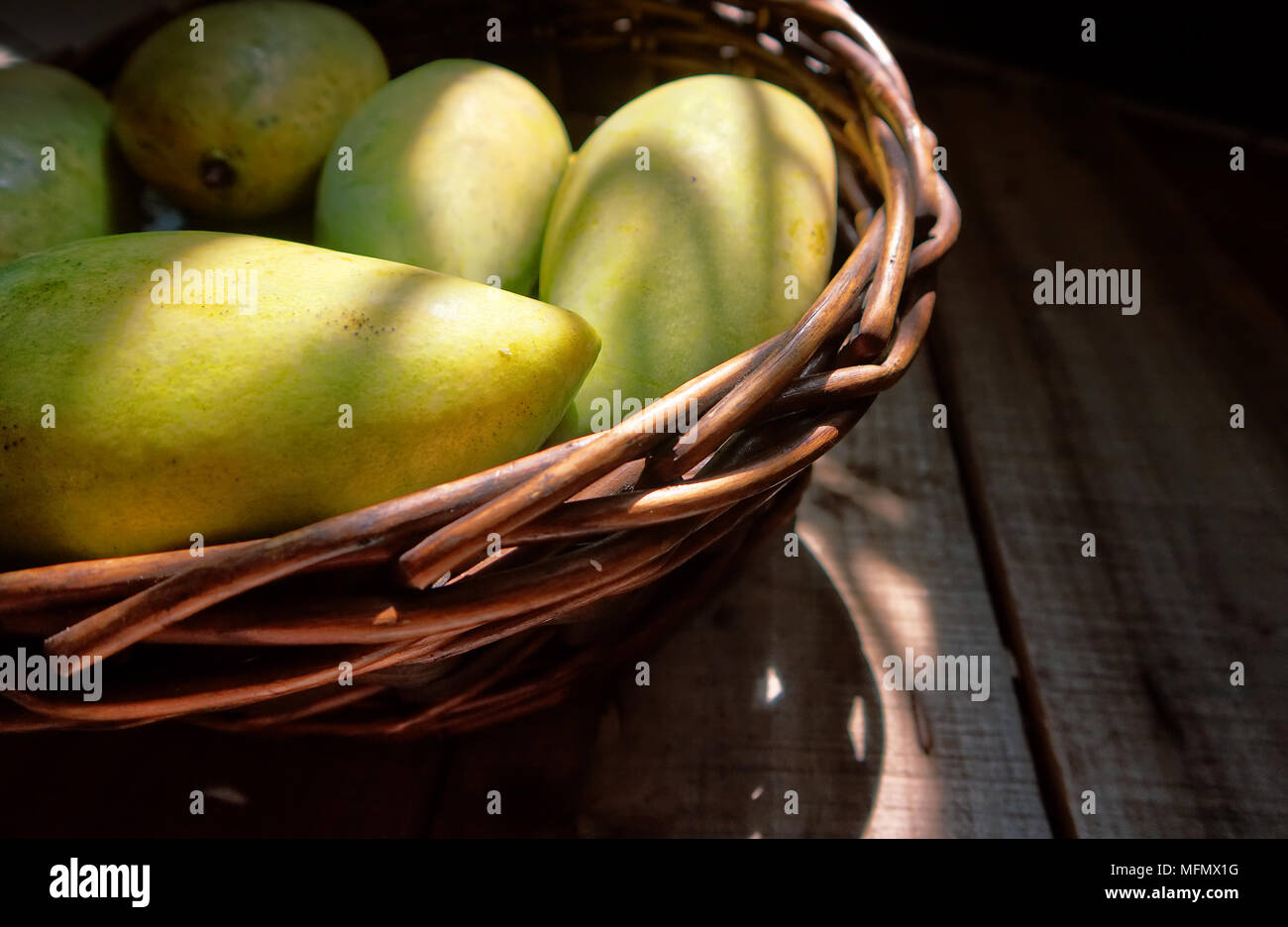 Mangoes in the basket on wood plate with sunlight from window. Stock Photo