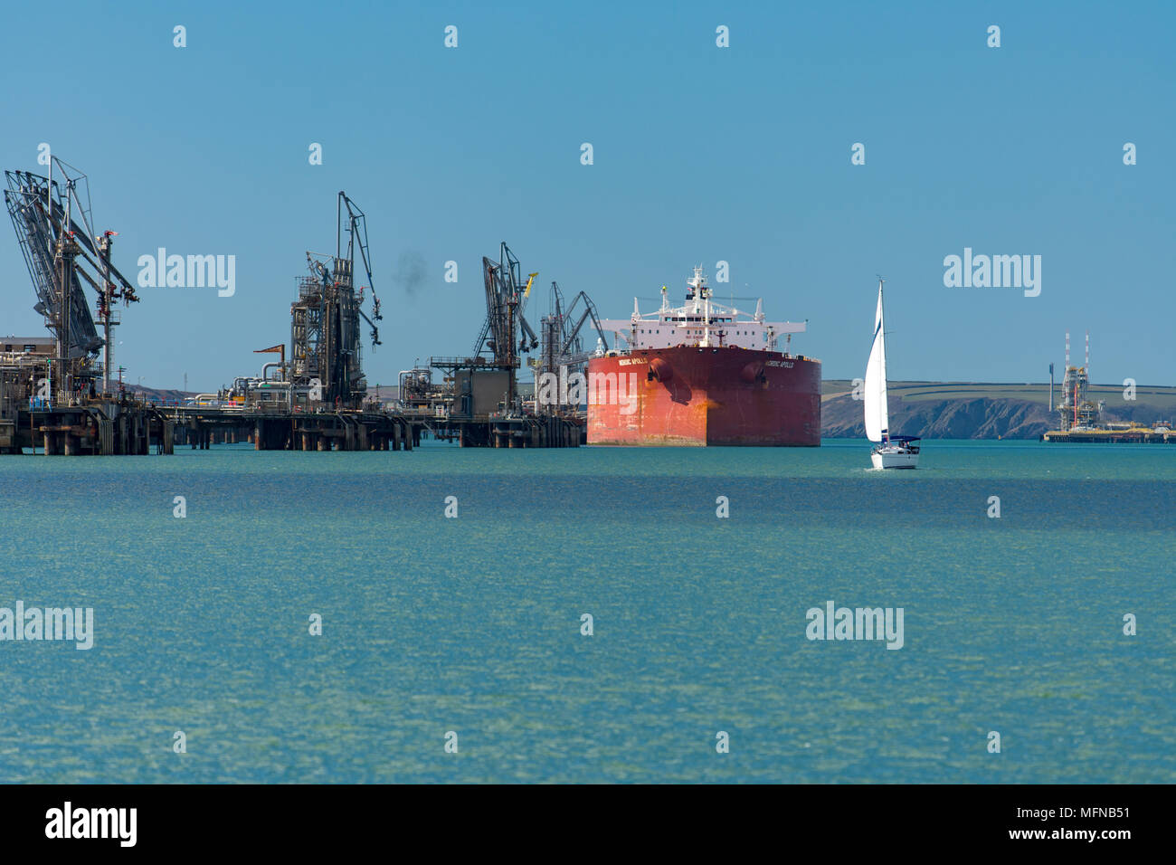 Yacht sailing with petrochemical industry behind Stock Photo