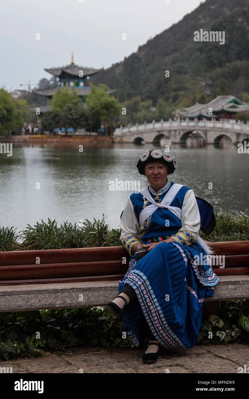 Lijiang, China - March 23, 2018: Chinese woman wearing a traditional Bai minority attire sitting in front of the Black Dragon Pool in Lijiang Stock Photo