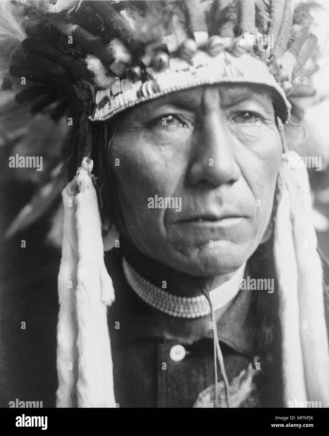 Head-and-shoulders portrait of a Nez Percé man in full feather headdress, 1910. Photograph by Edward Curtis (1868-1952). Stock Photo