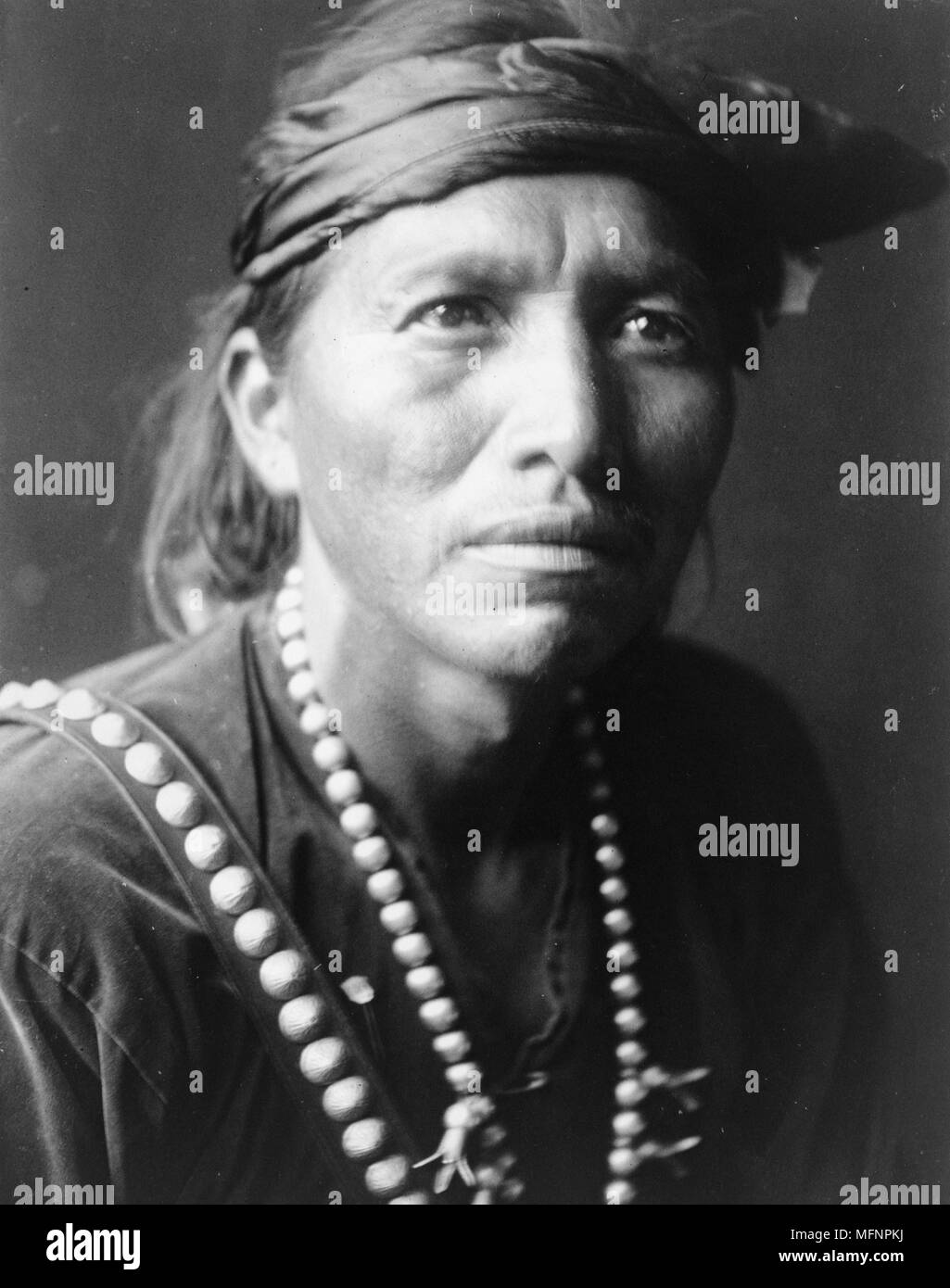 Head-and-shoulders portrait of Navajo man, facing slightly right, wearing headband and silver squash blossom necklace.1906. Photograph by Edward Curtis (1868-1952). Stock Photo