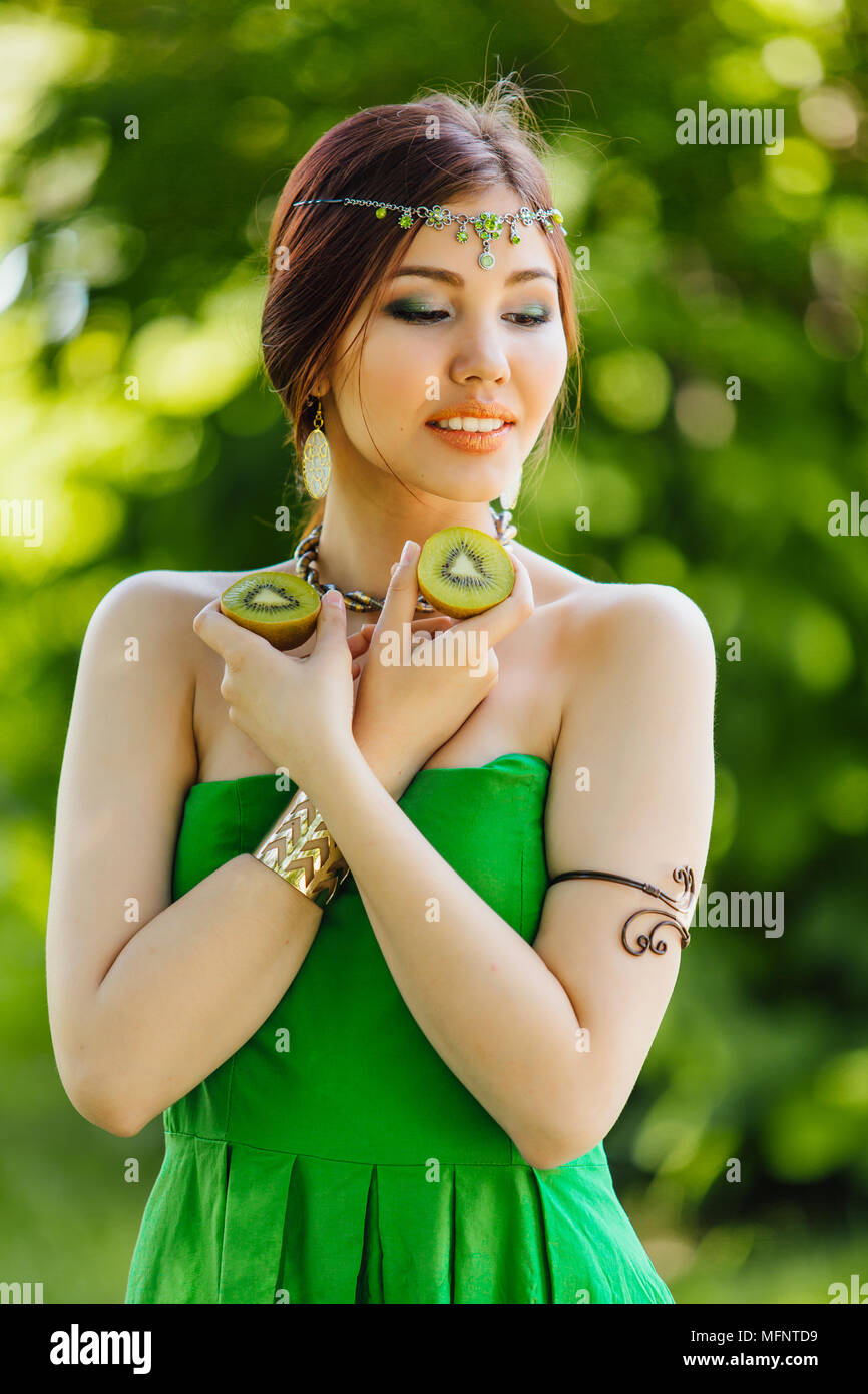 Portrait of a beautiful young asian woman holding two halves of kiwi ...