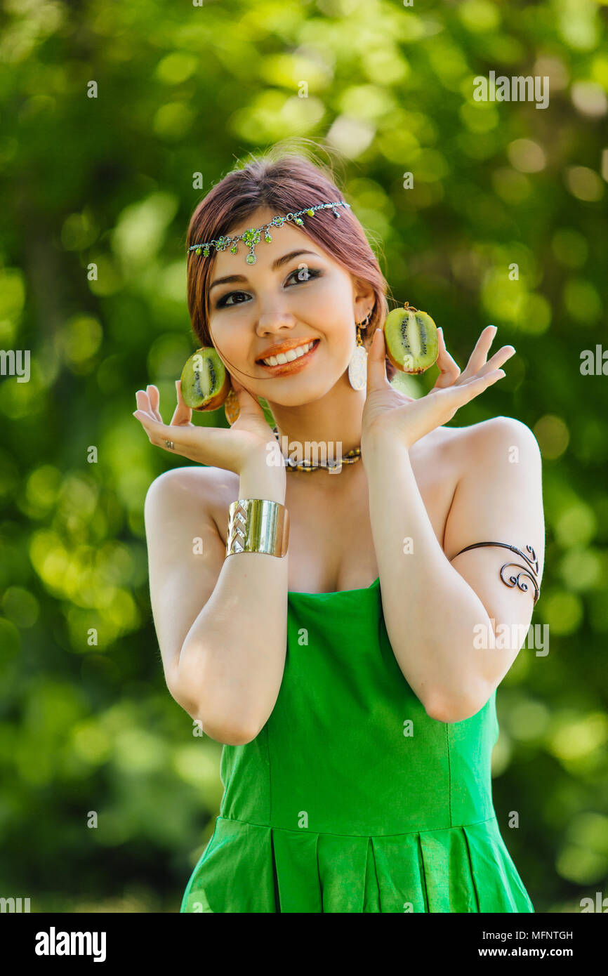 Portrait of a beautiful young asian woman holding two halves of kiwi ...
