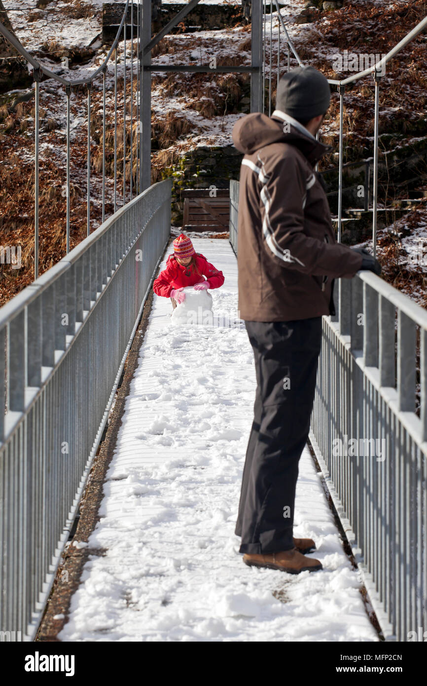 Father and daughter playing with snow on a suspension bridge in the Valle Onsernone, Ticino, Switzerland Stock Photo