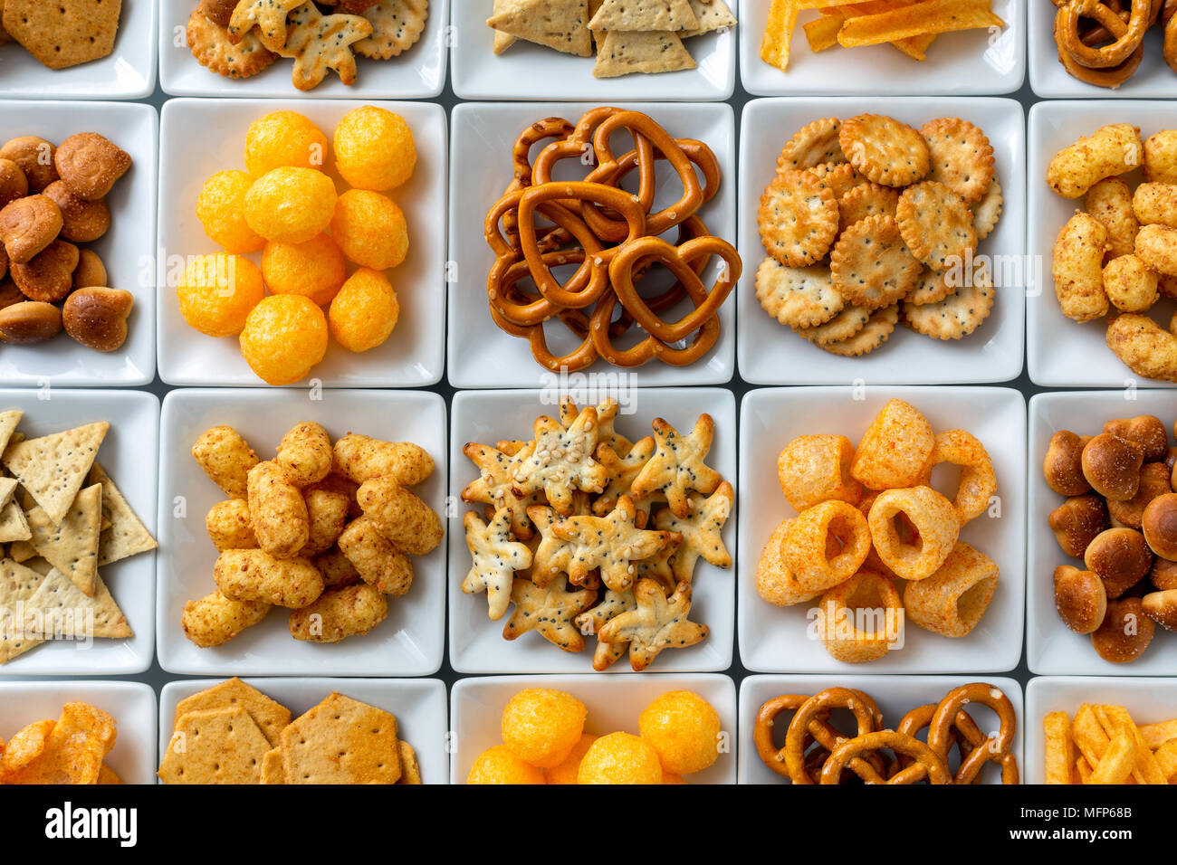 Background of many types of savory snacks in white square dishes from above. Stock Photo