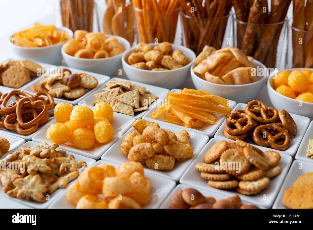 Rows of many types of savory snacks in white ceramic dishes. Stock Photo