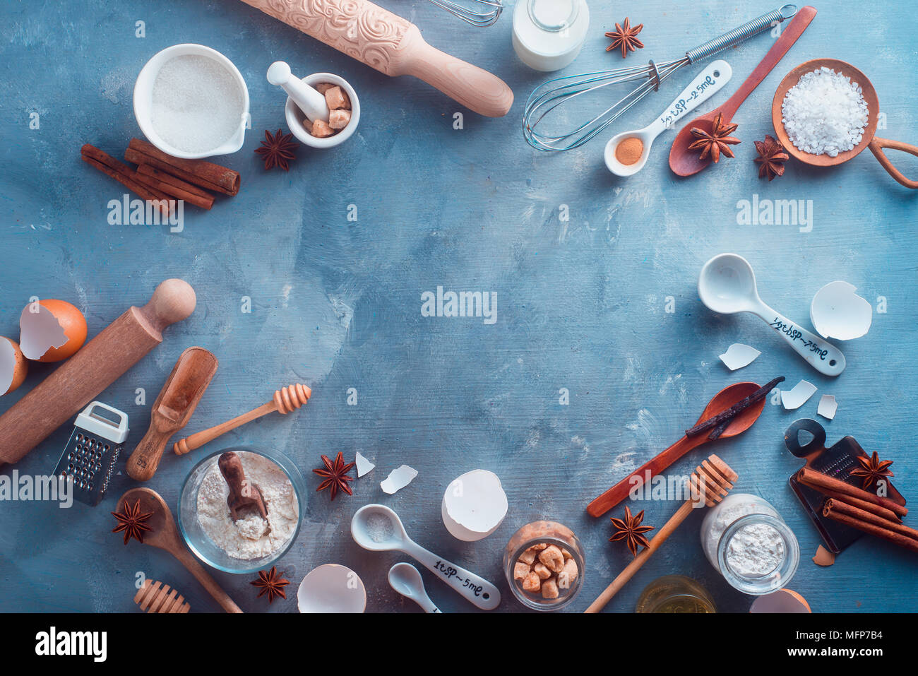 Cooking flat lay header with baking tools and ingredients. Rolling pin, whisk, honey spoon, milk bottle, butter, sugar, flour, cinnamon and eggs on a  Stock Photo