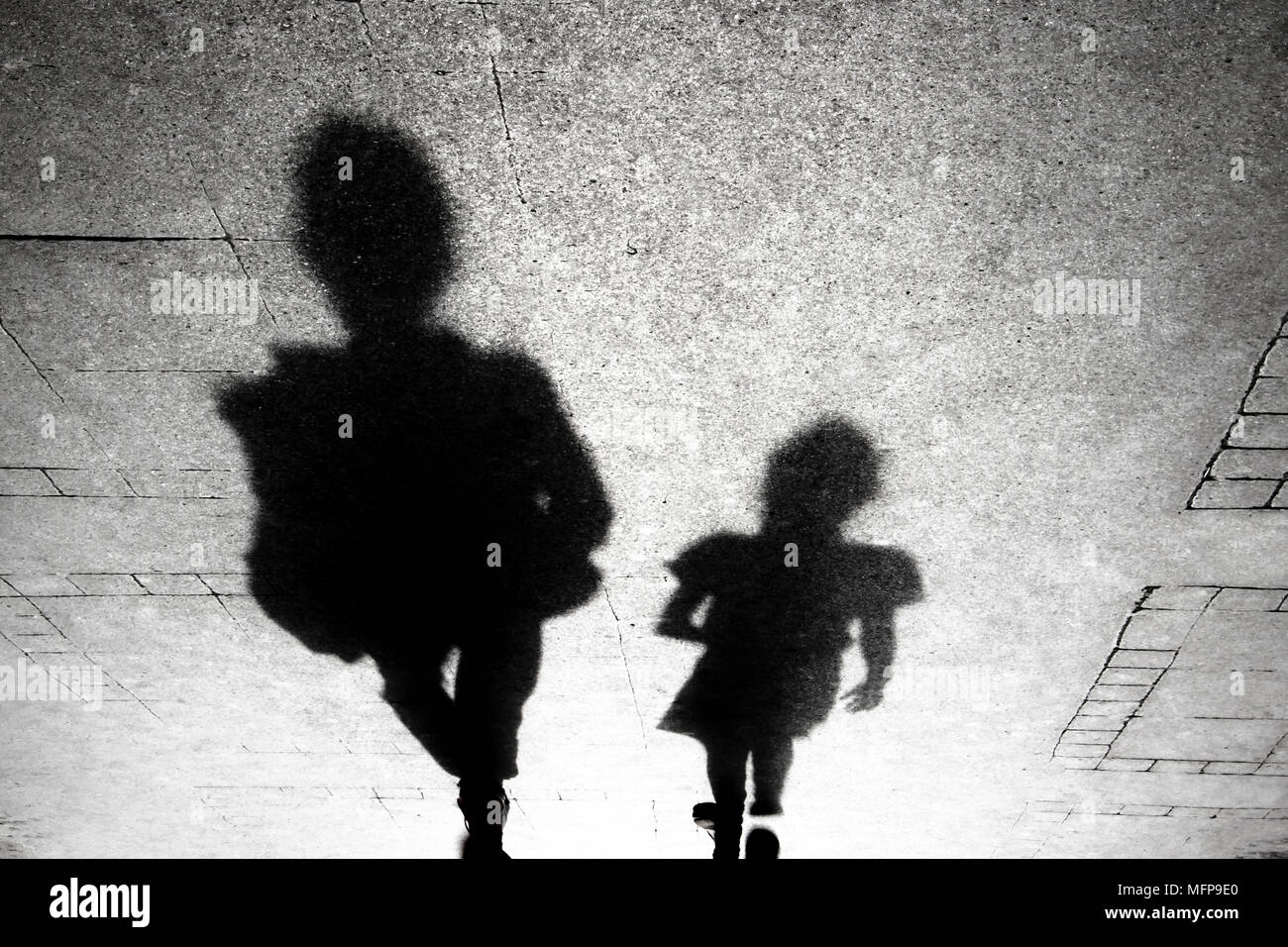 Shadow silhouette of an adult and a kid walking od the city sidewalk in  black and white Stock Photo