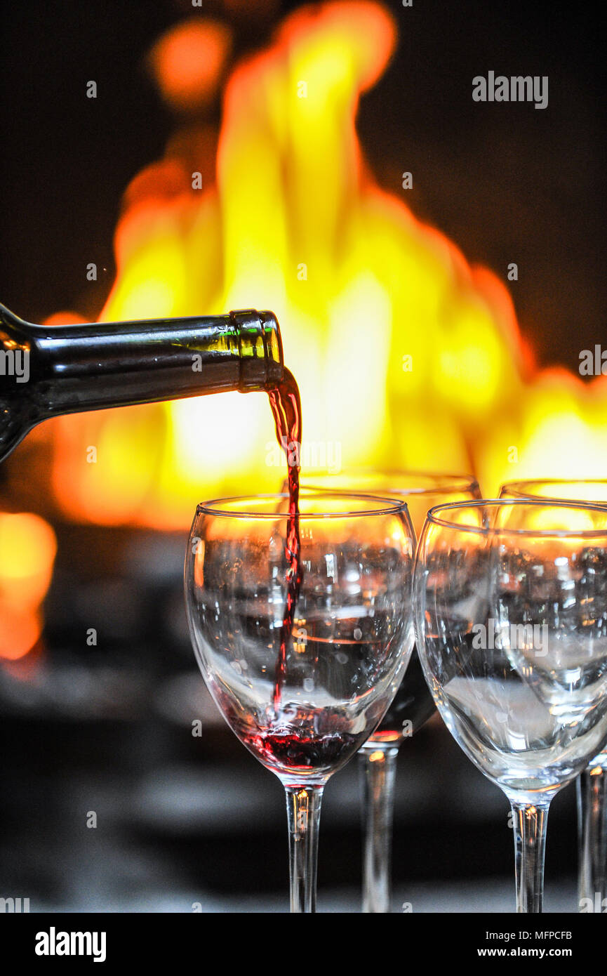 Red wine is poured into a glass in front of an open fire. Stock Photo