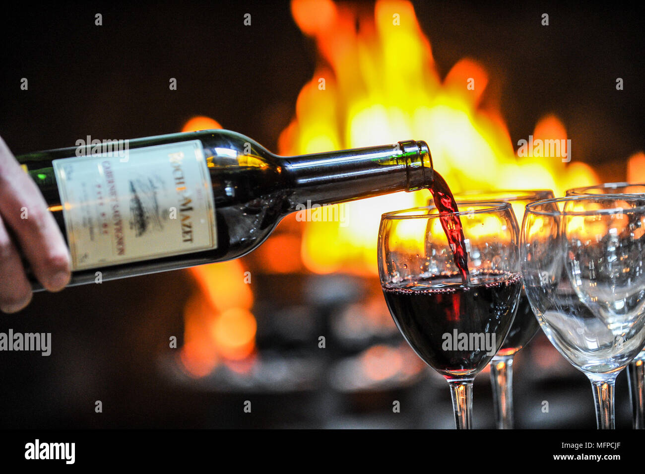 Red wine is poured into a glass in front of an open fire. Stock Photo