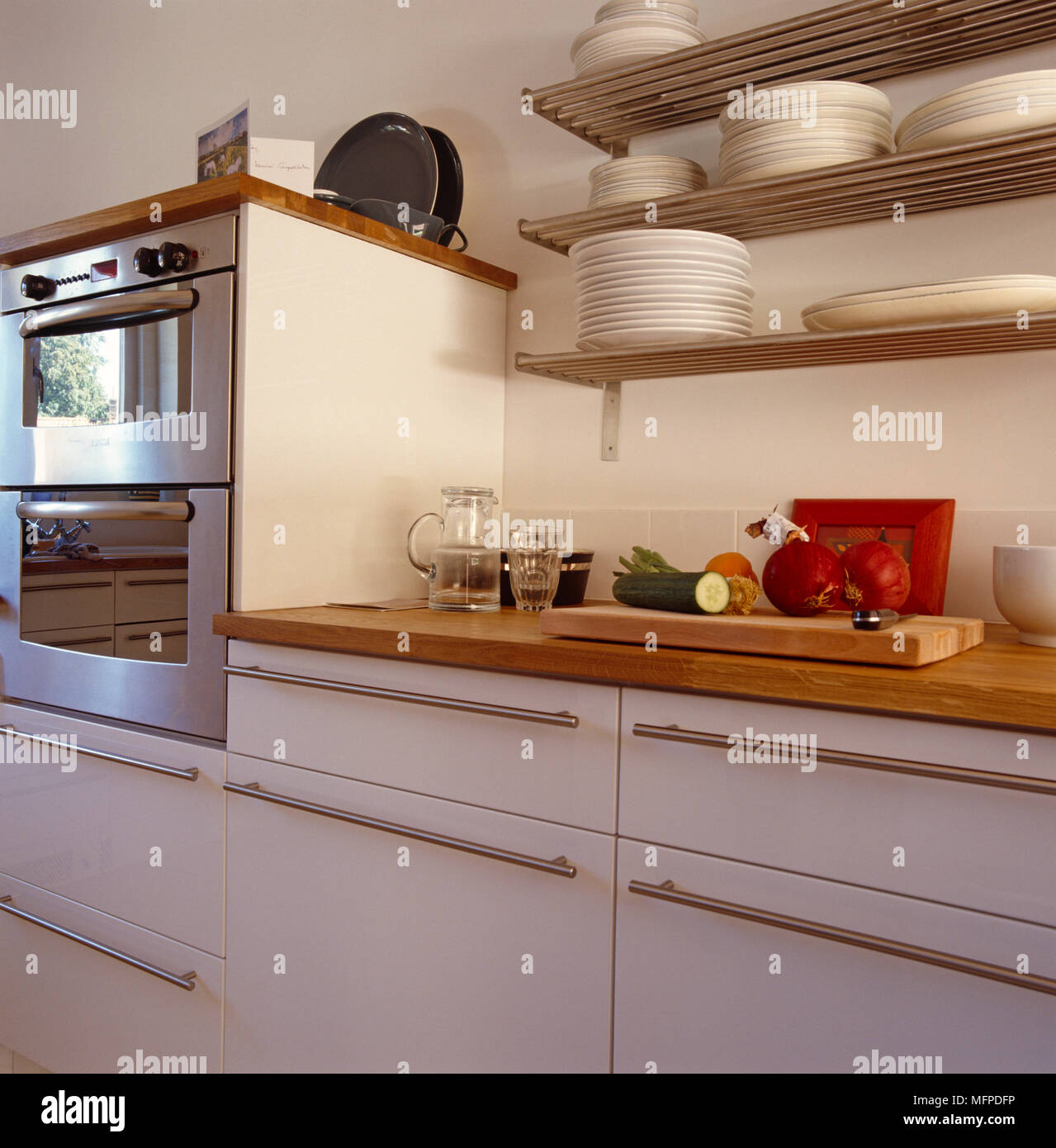 A small kitchen with stainless steel appliances, white cabinets, and a  natural light colored wood counter top Stock Photo - Alamy