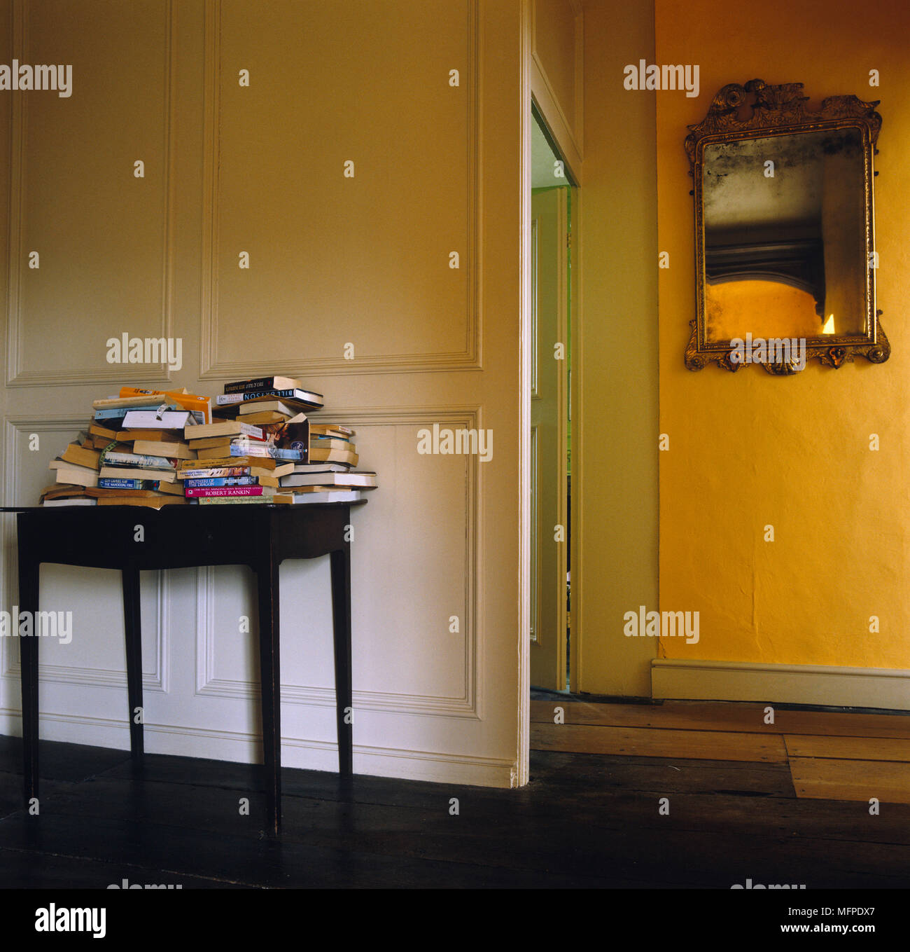 Wooden table laden with books in yellow hallway Stock Photo Alamy